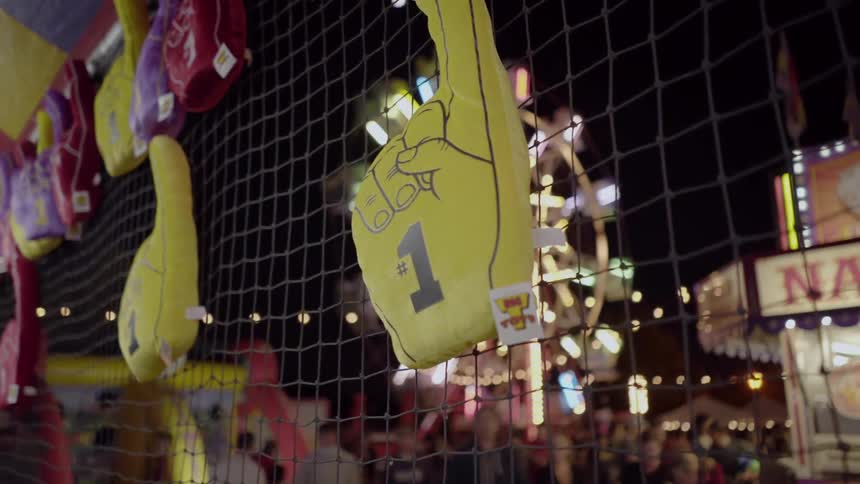 Yellow foam fingers are hanging on a wire fence at an amusement park