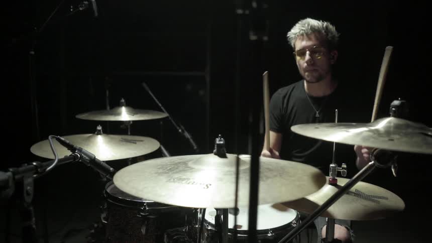 A man with shades sitting down playing the drums