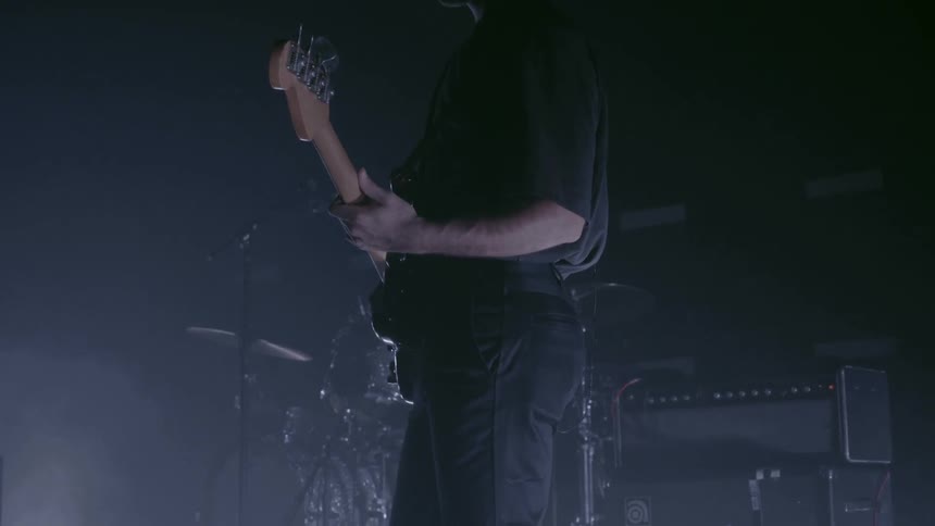 Man play a guitar in front of the drum set in a dark stage