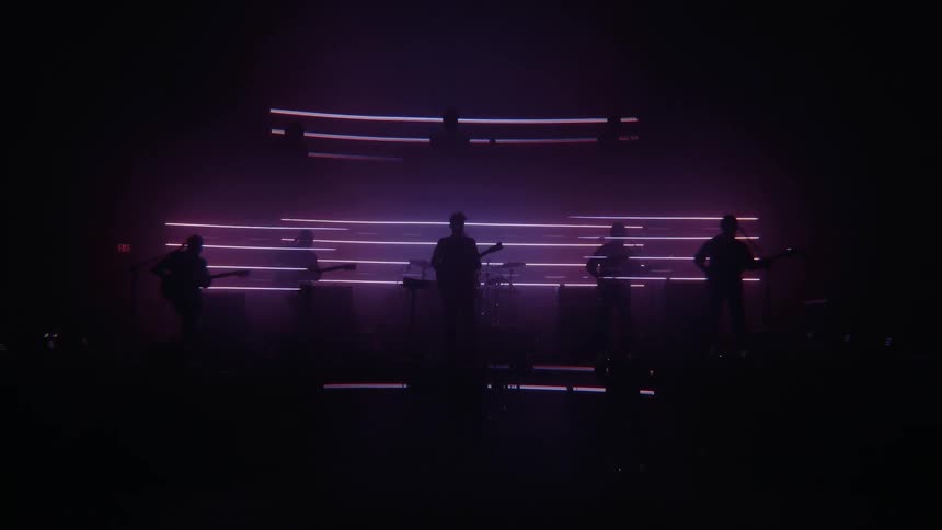 A rock band performs on a stage filled with neon lights
