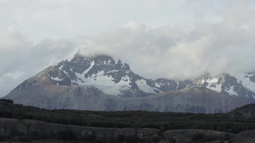Clouds hang over and cover a snow dotted peak