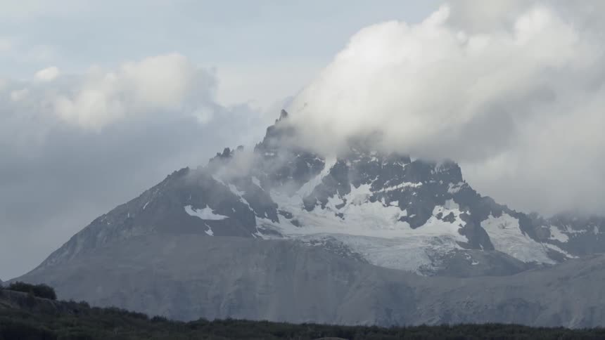 Clouds drifting past a snowy mountain peak