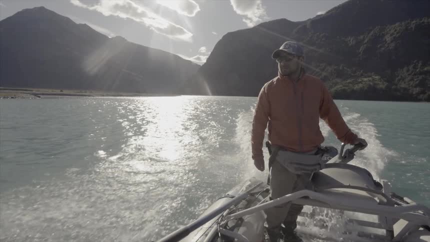 A man driving a boat across a lake surrounded by mountains
