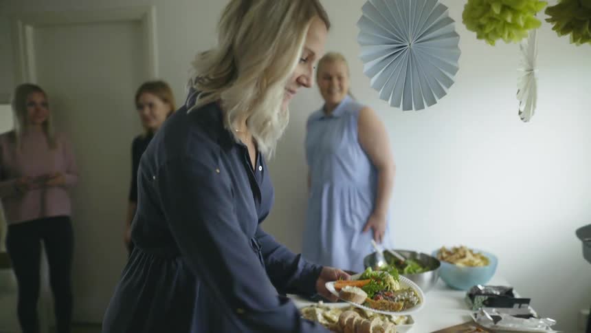 A blonde pregnant woman piles food onto a paper plate