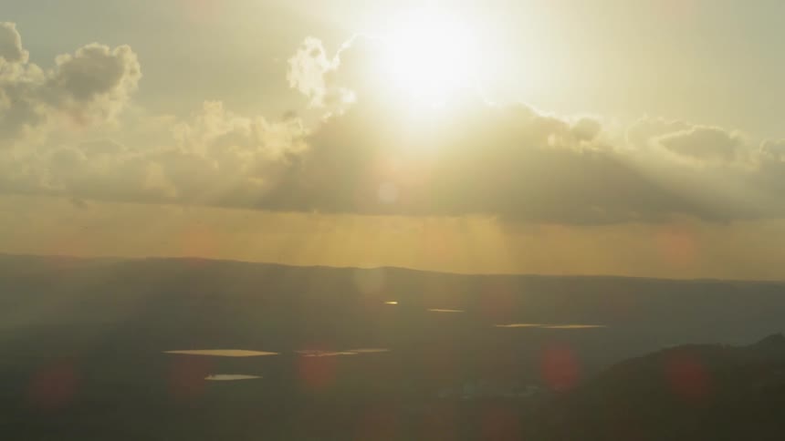 Sun glares through clouds over landscape
