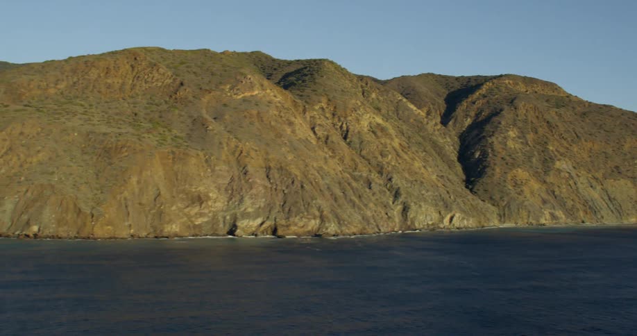 The camera pans over an ocean and looks at a rocky shoreline at day