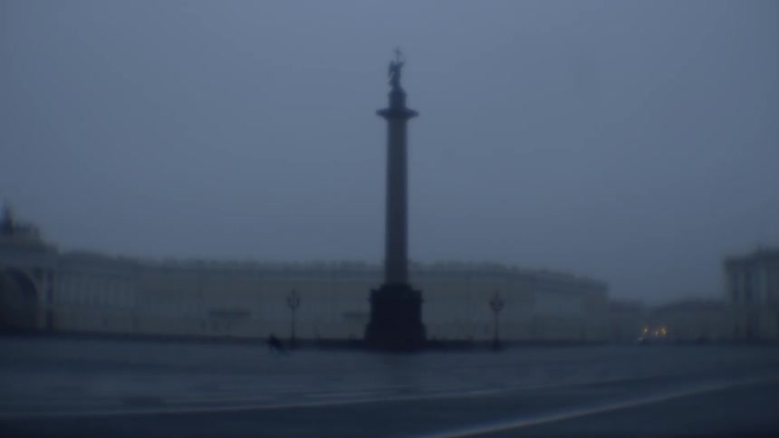 A person runs across a park containing a tall monument on a rainy day outside