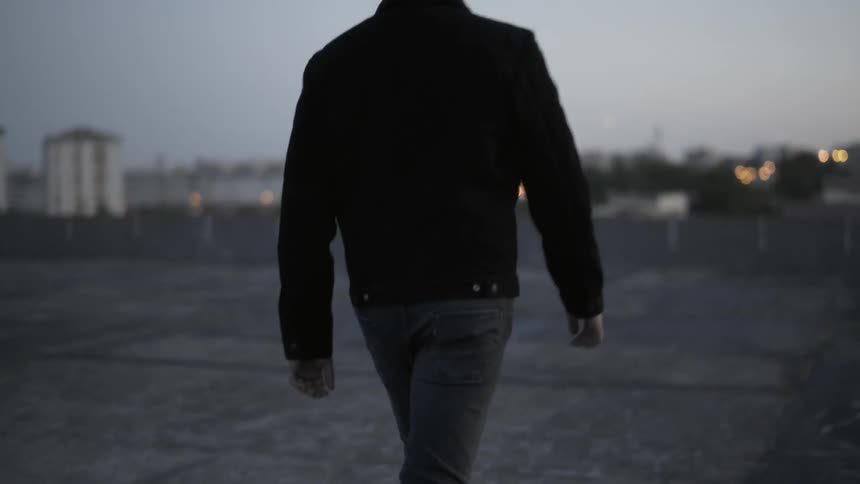 Man wearing denim jacket walks on the flat roof at dusk