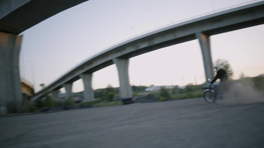 A motorcycle rider turns in the dirt under overpasses kicking up dust as he goes