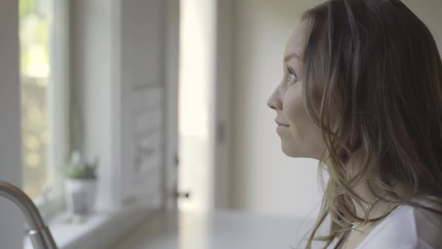 A white woman looks out a kitchen window
