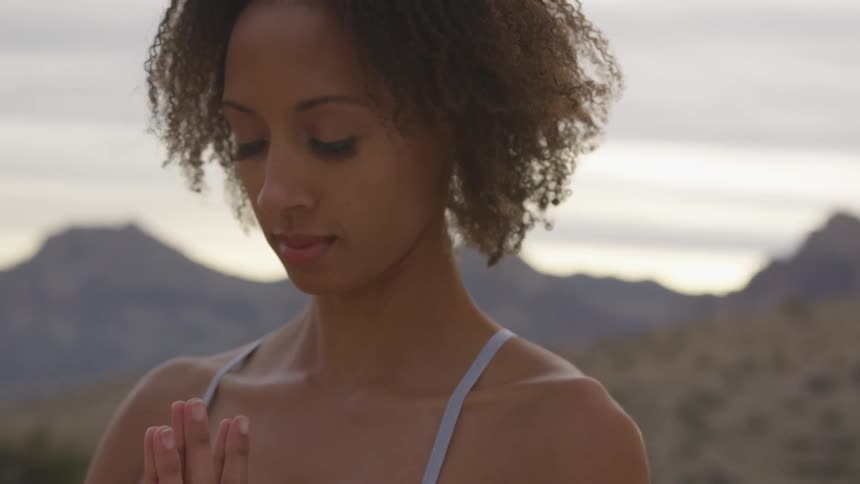 A woman is in the desert with her hands together meditating