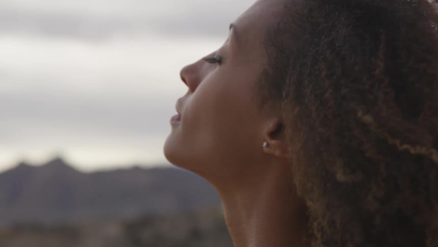 A woman stands outdoors on a cloudy day with her eyes closed
