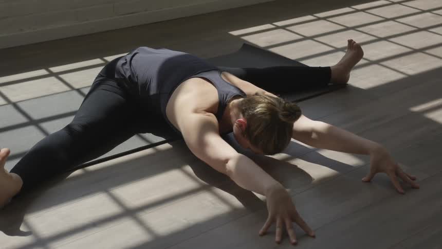 A woman with legs stretched out wide to the side and leaning forward