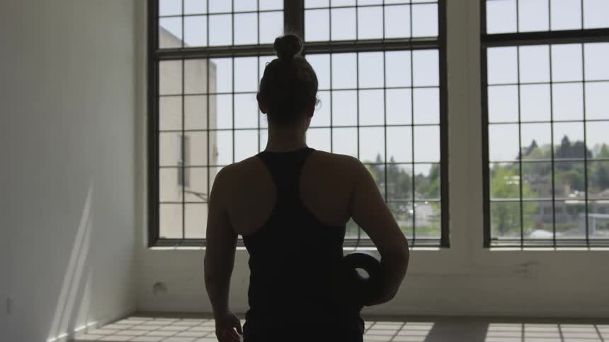 Woman carrying sport mat walks towards windows in the daytime