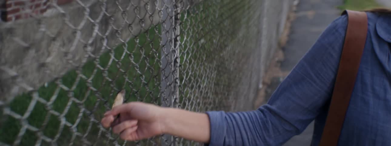 Woman trails her hand on a fence as she walks