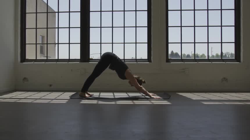 A woman does a yoga pose in front of windows in a fitness studio
