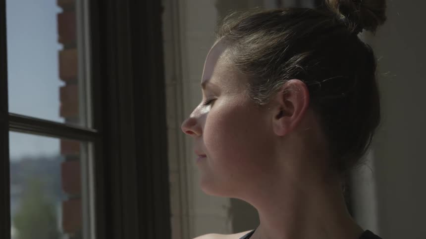 Woman standing near a window with eyes closed