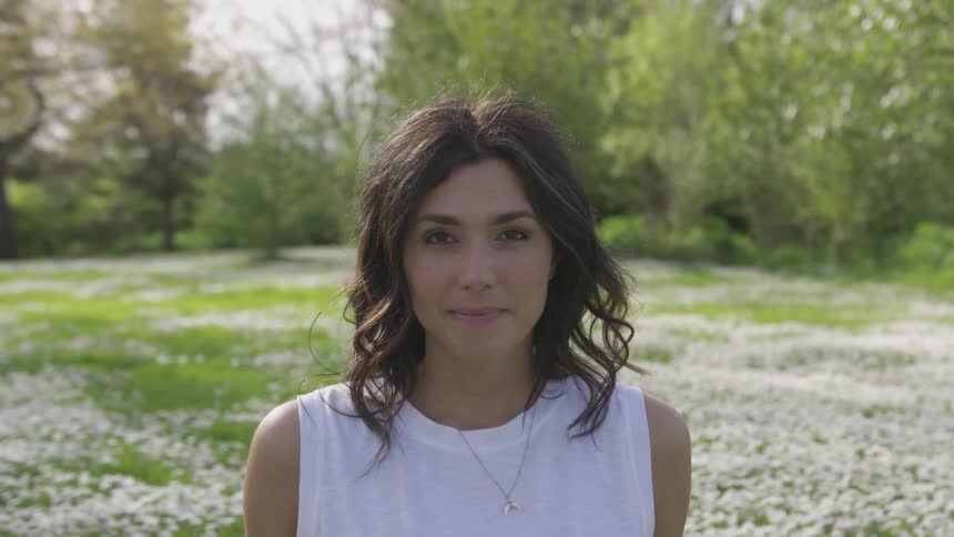 Brunette woman wearing white t shirt and necklace smiles in a flower garden in the daytime