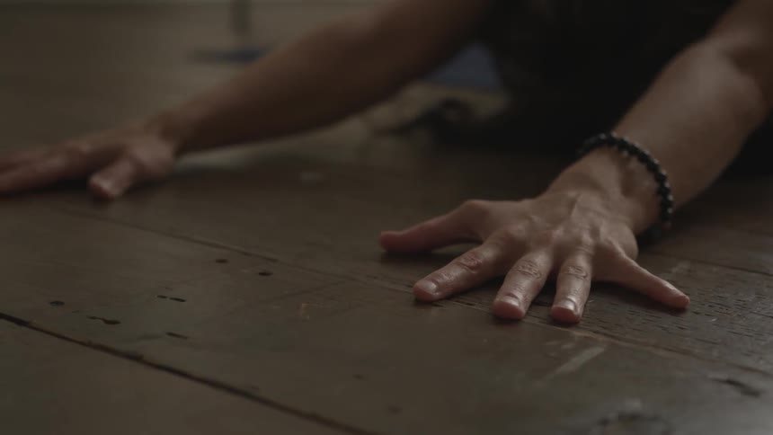 A woman is stretching her arms and fingers out onto a hardwood floor