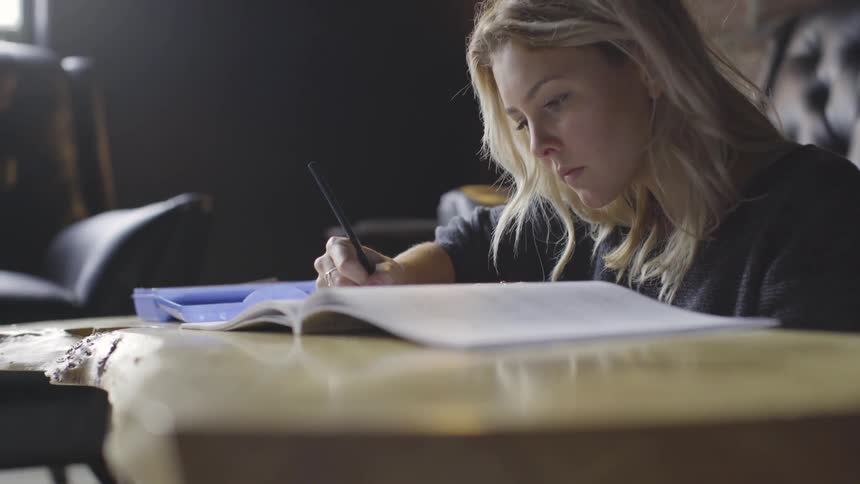 A woman writes in a notebook at a table