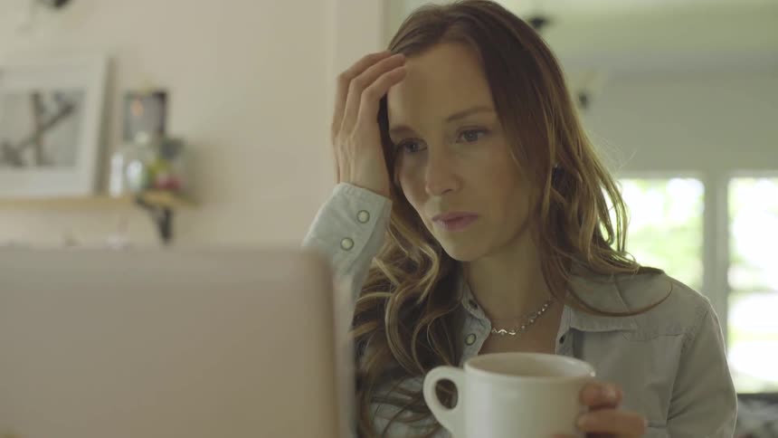 Woman reading on her computer screen while holding a cup