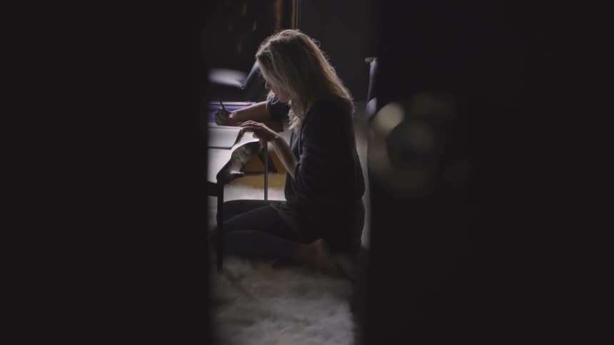 A white woman sits in front of a coffee table while writing in a book