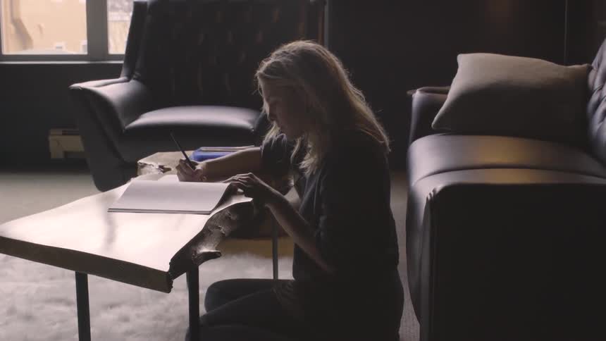 A woman is writing in a workbook on a coffee table while sitting on the floor