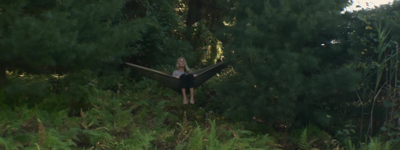 A woman sits on a hammock in the woods