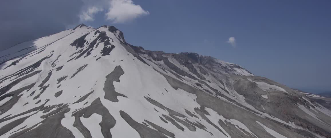 Aerial view of a snow covered mountain with a dark cloud on the left blue sky of the right