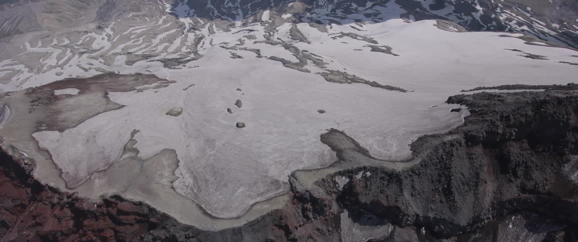 An enormous mountain gives way to a large slope that is covered in snow