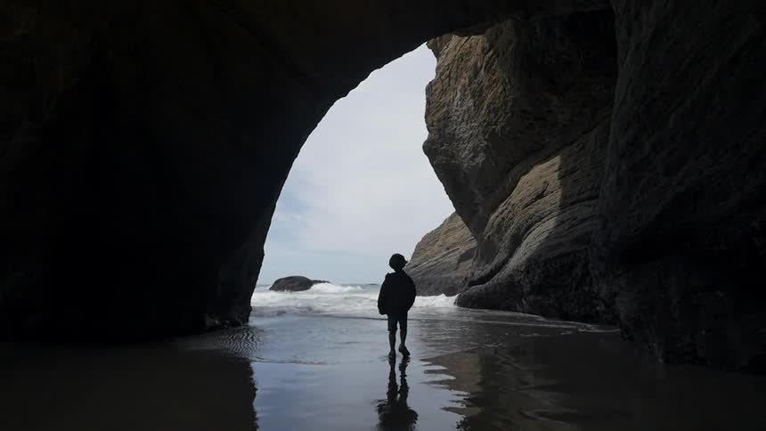 Child walks under a large rock formation towards a body of water