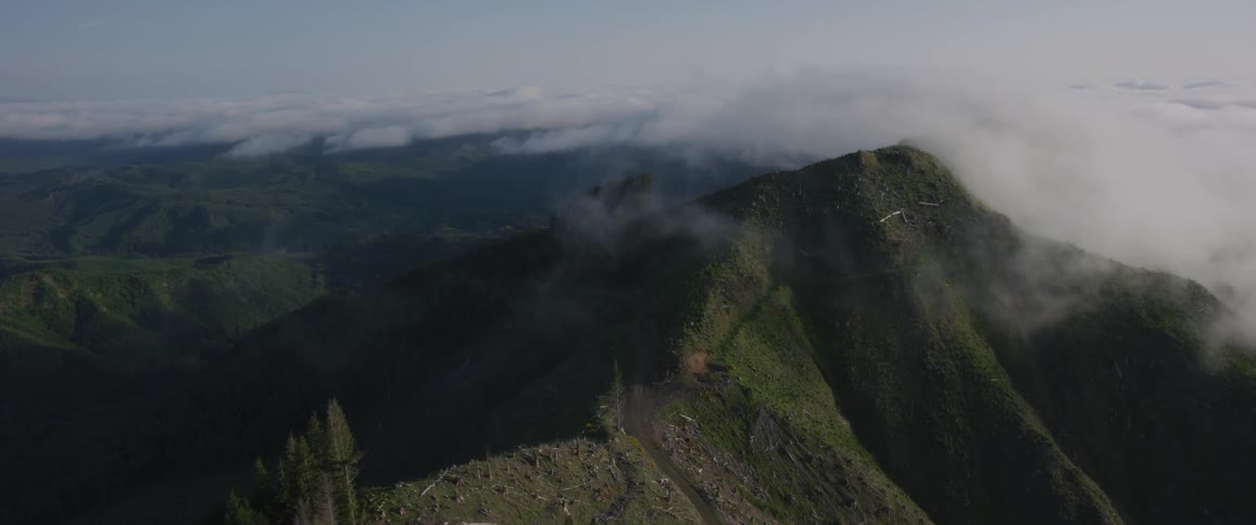 A grass covered mountain with clouds at its summit