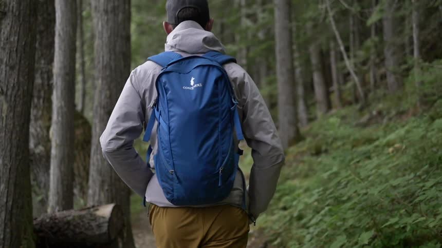 A man wearing a blue backpack walking through the woods