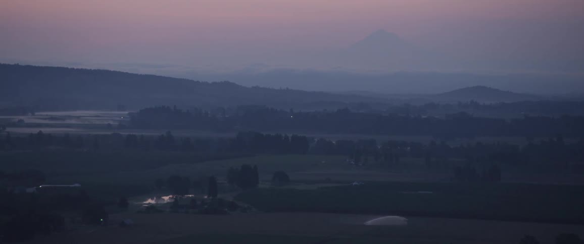 The camera flies across a hazy valley with mountains in the distance