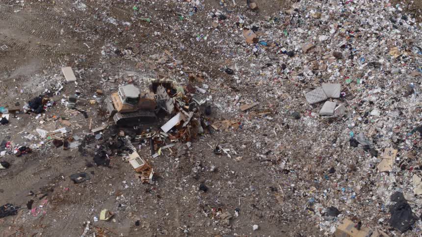 A heavy machine pushes garbage down a hill into a mound