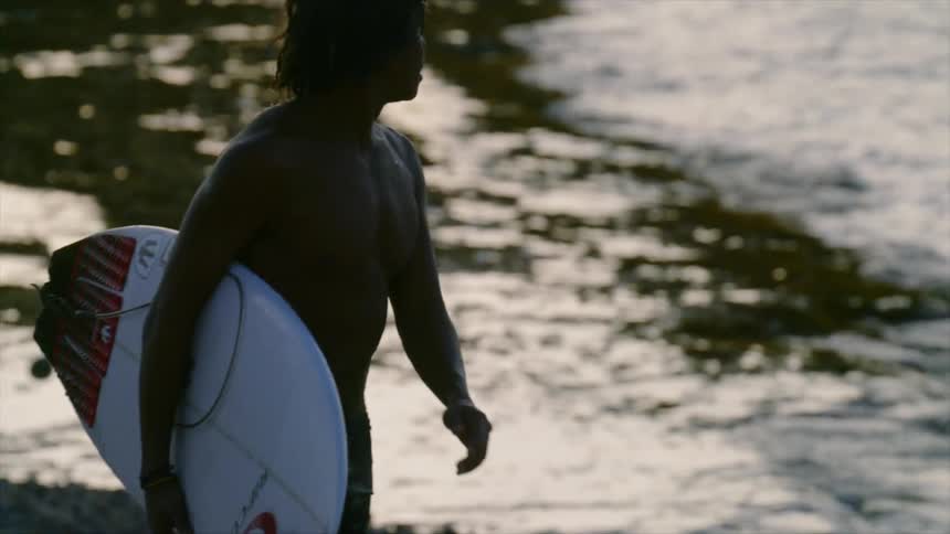 A young man walks down a beach carrying a surfboard