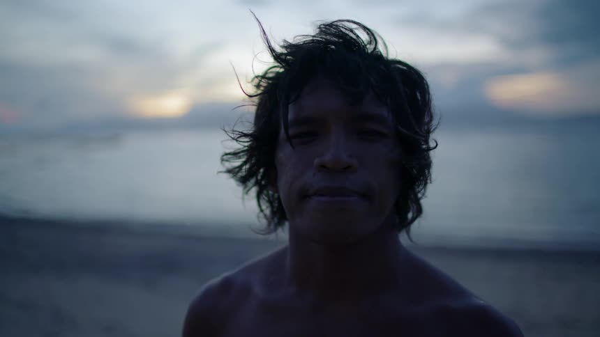 A person stands on the beach looking into the camera