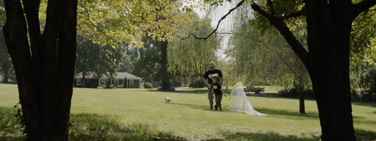 Father and son playing soccer on the grass next to a house