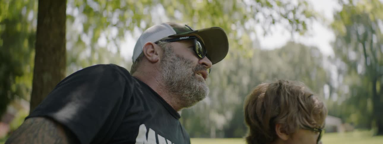 Man throws ball as he sits next to a boy in the park