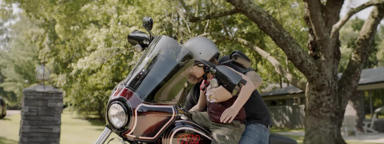 Man lifts boy onto motorcycle seat in front of him