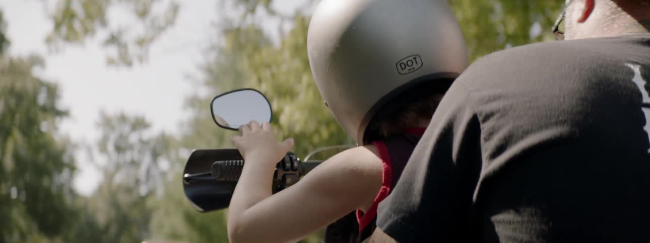 A nab helps a child onto his motorcycle then adjusts her and grabs the motorcycle handles