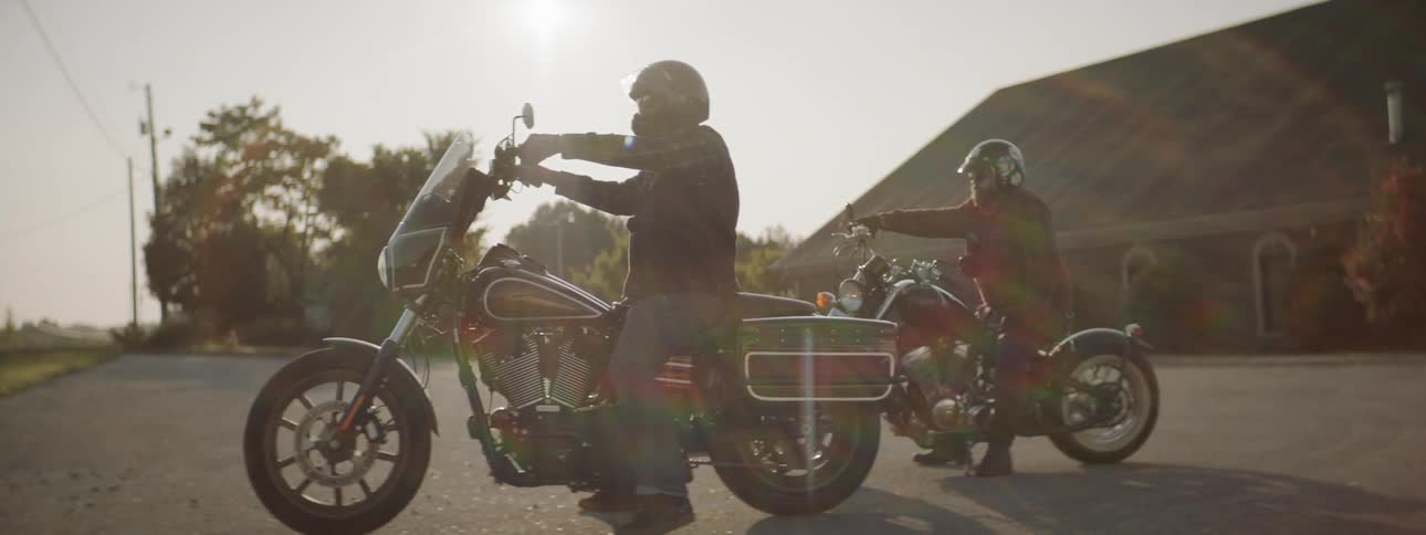Two friends sitting on their motorcycles in an empty parking lot in the countryside