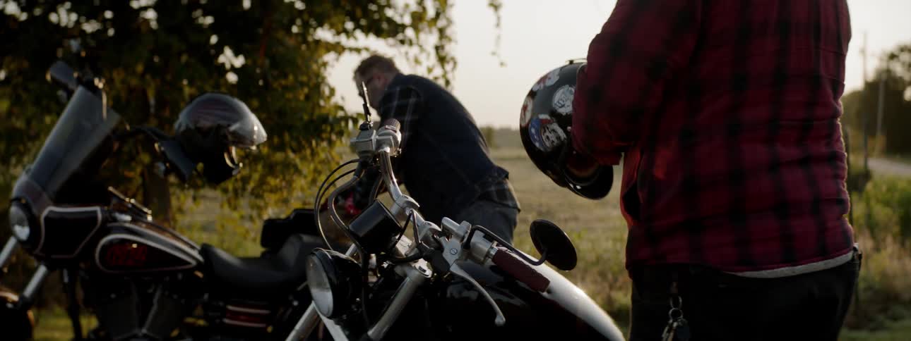 A man getting on a motorcycle while another digs in a trunk