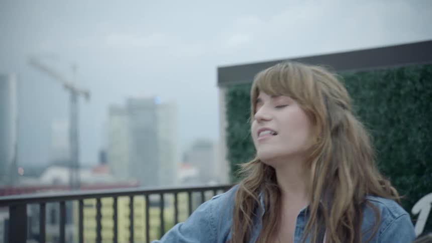 A young woman plays guitar outside in a city