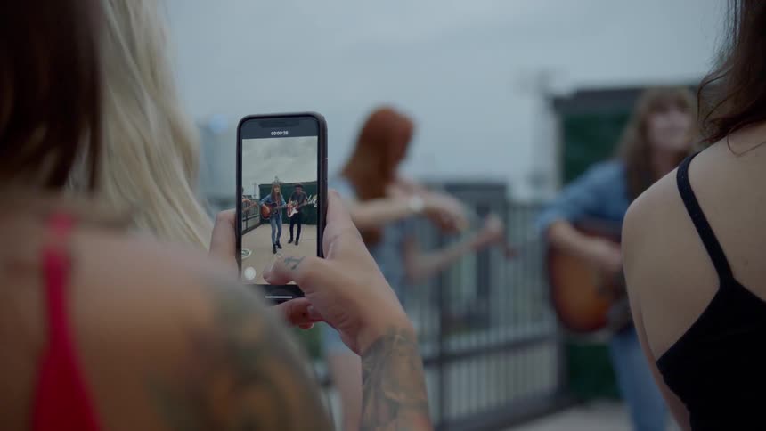 A woman talking a video with her smartphone of a group of musicians performing outdoors
