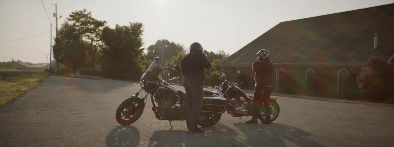 Two men get off of motorcycles and remove their helmets