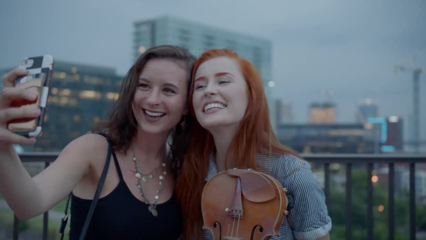 Two women pose for a selfie one of them holding a violin