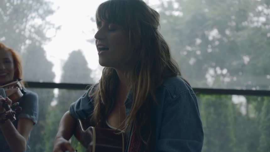 A woman strums a gibson acoustic guitar accompanied by a violinist