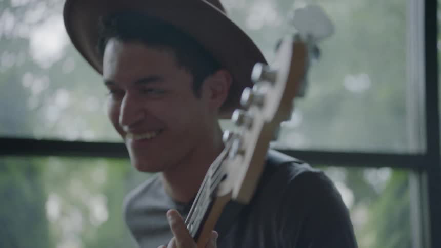 A hat wearing man plays the bass guitar and smiles