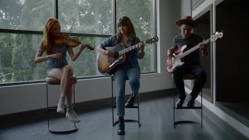 A violinist guitarist and bassist play together while sitting on stools